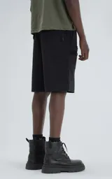 Bermuda técnica color negro, confeccionada en microfibra liviana, con cintura ajustable mediante cinturón integrado. Presenta múltiples bolsillos funcionales, incluyendo un bolsillo lateral con detalle de malla texturizada.