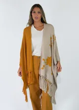 Ruana de punto bicolor, con un lado marrón y otro lado beige con detalle de bordado floral y flecos en los bordes inferiores.