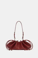 Mini bolso de hombro color bordó, con cuerpo fruncido, textura símil serpiente y tiras laterales ajustables. Cuenta con asa de hombro y cierre mediante fruncido.