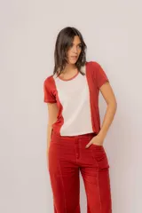 Remera de manga corta con diseño bicolor, combinando paneles en color terracota y un panel central en color crema. Presenta detalles de puntilla en las costuras laterales y un corte asimétrico, siendo más corta en la parte frontal.
