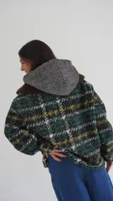 Buzo canguro oversize de paño de lana gris con capucha estampada y cuello de corderito blanco. Cuenta con aberturas laterales en el ruedo y detalles de cuero sintético marrón en el cierre frontal y etiqueta.