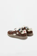 Zapatillas urbanas de cuero con paneles en gamuza negra y detalles en cuero color crema. Presentan suela de goma texturizada en tono marrón y cordones bicolores.