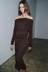Vestido largo de color marrón oscuro, con cuello fluido tipo bote, manga larga y detalle de fruncido lateral con broche metálico en la cintura.