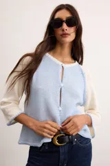 Saco de algodón tejido de punto con cuerpo celeste y mangas blancas, cuello redondo y cierre frontal con botones blancos.