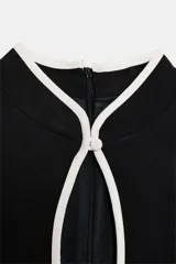 Vestido corto negro con cuello mao, abertura en el pecho y ribetes blancos en contraste. Cuenta con mangas cortas y cierre lateral con cremallera oculta.