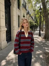 Sweater de tejido bremer con diseño a rayas horizontales en tonos bordó, azul marino y blanco. Presenta cuello polo en color crema y mangas largas con puños ajustados.