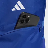 Mochila Adidas modelo Tiro, color azul con detalles en blanco. Cuenta con compartimento principal con cierre, bolsillos laterales de malla y correas acolchadas ajustables. Presenta el logo de la marca en la parte superior y las tres tiras características en la parte inferior frontal.