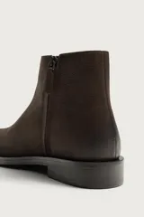 Bota de cuero color marrón oscuro con diseño de caña media, horma cuadrada y cierre lateral mediante cremallera. Cuenta con suela a contraste y un ligero tacón.