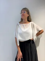 Poncho corto de gasa blanca, con escote amplio tipo barco y mangas amplias. Se lleva sobre otra prenda.