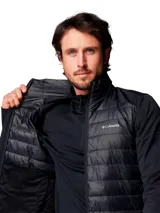 Chaqueta híbrida para hombre con cuerpo acolchado y mangas de tejido softshell liso. Presenta cierre frontal completo, cuello alto y logo de la marca estampado en el pecho. Diseñada con tecnología repelente al agua y aislamiento térmico sintético.