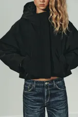 Cazadora acolchada de color negro con capucha, cuello subido y cierre frontal con cremallera y botones metálicos. Presenta manga larga con puño elástico, bolsillos delanteros y bajo ajustable con stoppers.