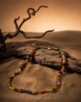 Collar largo de diseño artesanal compuesto por una variedad de cuentas de piedras naturales y materiales orgánicos en tonos tierra, naranja, verde y violeta, con cierre metálico.