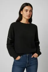 Sweater negro de punto con cuello redondo, corte holgado y detalle de tachas metálicas a lo largo de los hombros y mangas.