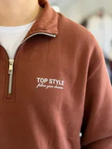 Buzo marrón de felpa con medio cierre y cuello alto, manga larga y puños elásticos. Presenta el texto "TOP STYLE follow your dreams" bordado en el pecho.