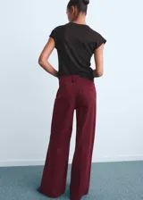Pantalón de jean estilo wide leg, color bordó, con tiro alto, cinco bolsillos, cierre frontal con cremallera y botón, y trabillas para cinturón.