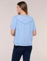 Blusa celeste de lyocell ultraliviano, de estilo romántico y silueta holgada. Presenta escote redondo con abertura en V y botones frontales, canesú fruncido y mangas cortas amplias.