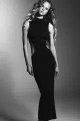 Vestido largo de corte recto con cuello perkins y diseño sin mangas. Presenta aberturas laterales (cut out) en la cintura con detalles de aplicaciones de pedrería tipo joya.