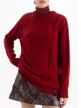 Sweater de punto color rojo con diseño de trenzas verticales y textura estructurada. Presenta cuello redondo, mangas largas y un corte holgado con terminaciones acanaladas.