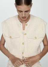 Chaleco color crema con textura tweed, cuello redondo, cierre frontal con botones dorados y dos bolsillos de parche con botón.