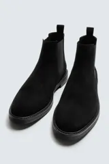 Bota estilo Chelsea de hombre, confeccionada en piel con acabado de serraje en color marrón. Presenta elásticos laterales oscuros para facilitar el calce, horma redonda y suela a tono con un ligero tacón.
