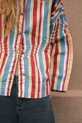 Camisa de denim azul con cuello mao, diseño holgado, mangas largas y cierre frontal con botones metálicos. Cuenta con costuras decorativas pespunteadas en el delantero.