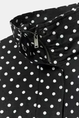 Cazadora negra con estampado de lunares blancos, cuello subido, manga larga, bolsillos delanteros, bajo ajustable con cordones y cierre frontal con cremallera y solapa con botones ocultos.