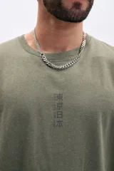 Remera verde militar de corte holgado con cuello redondo y mangas cortas. Estampa frontal con texto vertical en japonés y un dragón.