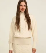 Suéter de manga larga confeccionado en tricot, con cuello alto y diseño de bordado de rombos en relieve. Presenta puños y cintura con terminación en tejido acanalado.