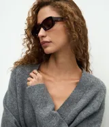 Cardigan de punto color beige con escote en V, cierre frontal con botones grandes y mangas largas con puños acanalados. Presenta un corte recto y estructurado.