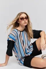 Remera oversize de manga corta con diseño de rayas verticales en tonos rojos, negros, blancos y tostados, y mangas blancas lisas.