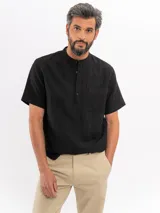 Camisa de manga corta negra de 100% algodón, con cuello mao, cierre frontal parcial con botones y un bolsillo en el pecho.