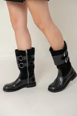 Bota de caña media combinada en cuero liso y gamuza, color negro. Presenta un diseño con doble hebilla lateral metálica y cierre de cremallera vertical en el lateral interno. Cuenta con suela plana y tacón bajo.