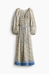 Vestido túnica largo de mezcla de viscosa, con diseño estampado floral en tonos azules y amarillos. Presenta escote en V con frunces, mangas globo con puños elásticos y un cordón fino ajustable en la cintura.