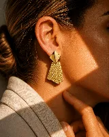 Aros colgantes de diseño geométrico en color dorado, compuestos por una pieza superior en forma de rombo liso y una pieza inferior trapezoidal con textura de cuadrícula grabada.