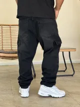 Pantalón tipo cargo de denim color negro con efecto lavado. Presenta corte holgado, bolsillos laterales con solapa y costuras reforzadas en las rodillas.