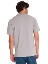 Remera tipo polo de manga corta color gris melange, con cuello de punto acanalado y tapeta con botones. Presenta el logo de CAT estampado en el pecho y un pequeño detalle bordado en color amarillo en la manga.