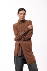 Polera de tejido de punto color marrón, con cuello alto y diseño de trenzas verticales. Presenta mangas largas con puños ajustados y un detalle de panel lateral asimétrico que se anuda en la cintura.