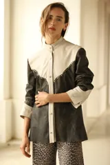 Camisa de cuero color negro y beige con corte a la cadera, cuello mao, cierre frontal con botones y detalle de tachas metálicas en el canesú.