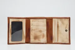 Billetera tríptica de cuero genuino en tono terracota con efecto desgastado. Cuenta con múltiples ranuras para tarjetas, un compartimento transparente para identificación y cierre con broche a presión.