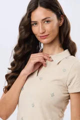 Remera polo de algodón color beige con mangas cortas, escote en V y cuello camisero. Presenta delicados mini bordados florales distribuidos en toda la prenda.