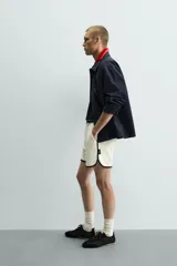 Short deportivo de tejido de punto con estructura abierta, color blanco con vivos a contraste en azul marino. Presenta cintura elástica, bolsillos frontales, aberturas laterales en el bajo y etiquetas conmemorativas de la Copa Mundial de la FIFA Francia 98.