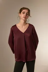 Blusa de satén color bordó con cuello en V y mangas tres cuartos. Presenta un diseño holgado con un pliegue central en el frente.