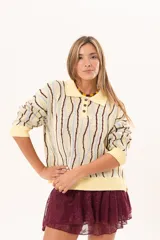 Buzo de punto tipo polo en tono amarillo claro con diseño de ondas a rayas en tonos marrón y celeste. Presenta cuello clásico, cierre frontal parcial con botones y silueta relajada con mangas largas.