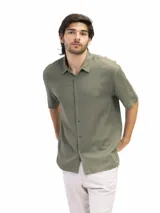 Camisa de manga corta color verde oliva, confeccionada en lino y viscosa, con cuello clásico y cierre frontal con botones. Corte suelto y estilo casual.