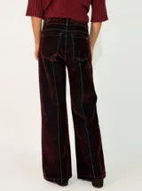 Pantalon de corte recto y tiro medio, confeccionado en denim con acabado aterciopelado en tono marrón oscuro. Presenta costuras verticales marcadas en contraste y cierre frontal con botón y cremallera.