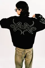 Sweater reversible de tejido de punto con diseño gráfico estilo tribal. Un lado presenta base negra con detalles en gris, mientras que el otro lado presenta base gris con detalles en negro. Posee cuello redondo, mangas largas y puños acanalados.
