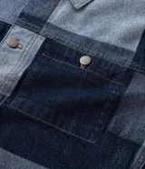 Campera de jacquard de algodón con diseño patchwork de cuadros en tonos azules. Presenta cuello inglés, cierre frontal con botones metálicos, mangas largas y bolsillos delanteros.