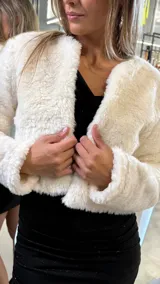 Chaqueta corta de piel sintética en color blanco, con diseño de manga larga y corte abierto sin cierre frontal.