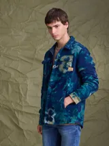Sobrecamisa de tejido polar con estampado abstracto en tonos rojizos y azul marino. Presenta cuello clásico, cierre frontal con botones a presión, dos bolsillos frontales con solapa en el pecho y un parche decorativo.