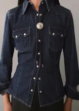 Camisa de denim azul oscuro con corte entallado, cuello camisero, cierre frontal con botones a presión, dos bolsillos con solapa en el pecho y mangas largas con puños abotonados. Incluye bolo tie con dije plateado y turquesa.
